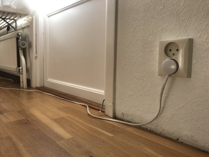 Uttag med tunn elektrisk kabel längs vägg och golv nära element.