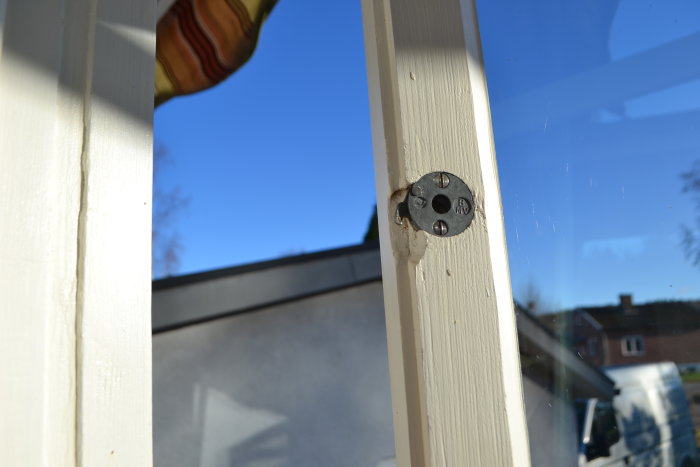 Synlig rund koppelhake på fönsterkarm i stängt läge, mot bakgrund av blå himmel.
