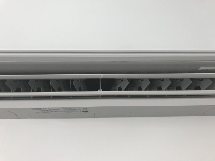 Toshiba luftkonditioneringsenhet monterad på en vit vägg med synliga fläktblad inställda för att dirigera luftflödet.