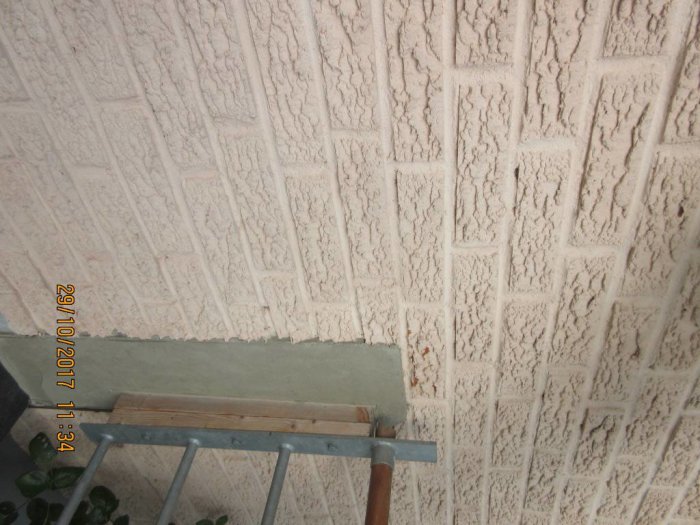 Råhuggen tegelfasad målad i ljusrosa färg med en liten provyta av slätputs i hörnet.