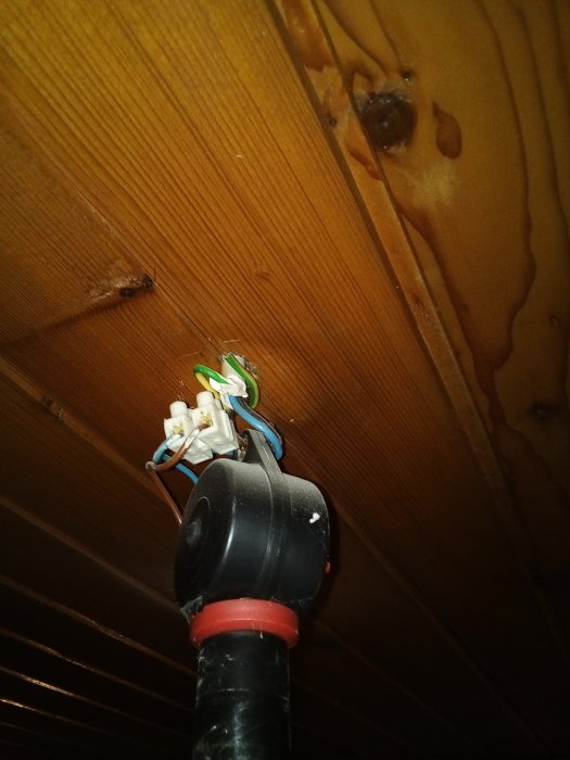 Takdosa för höj- och sänkbar lampa med synliga anslutna kablar och öppen kabelsko mot trävägg.