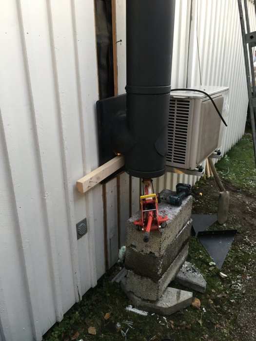 Skorsten höjd med domkraft ovanpå betongklack med tilluftsrör och värmepump intill.