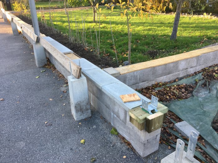 Pågående bygge av en mur med betongblock och träbjälkar vid en trädgårdsväg omgiven av höstlöv.