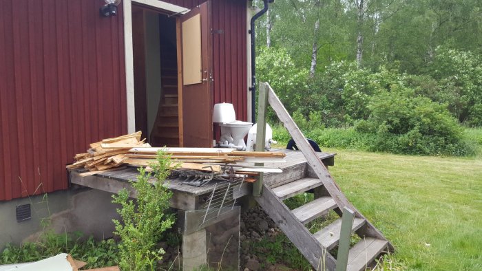 Renoveringsmaterial och toalettstol framför hus i rivningsfas med natur i bakgrunden.