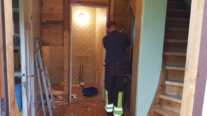 Renovering pågår i hus: person arbetar med dörröppning bredvid en trätrappa.