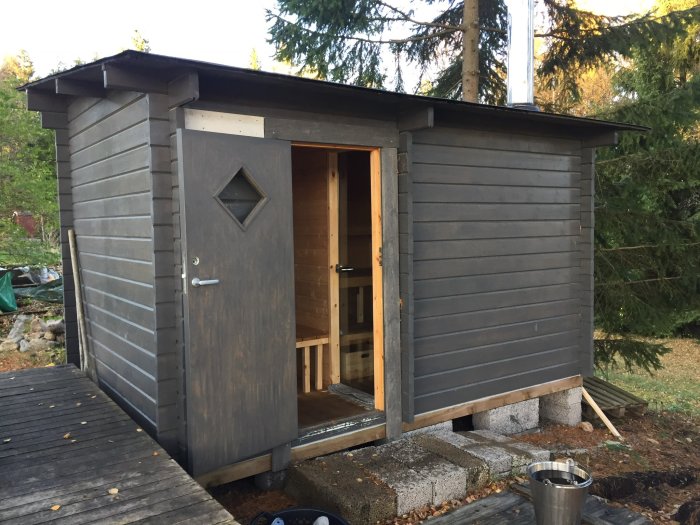 Knuttimmrad vedeldad bastu med öppen dörr och synlig interiör, belägen i lantlig miljö.