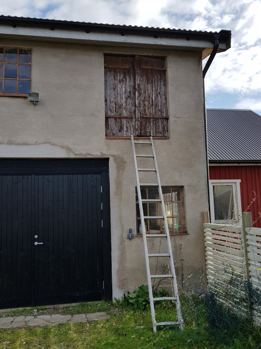 Tikkaat nojaavat kaksikerroksisen rakennuksen seinää vasten puuoven alla; toinen ikkuna näkyvissä, puuaita edessä.