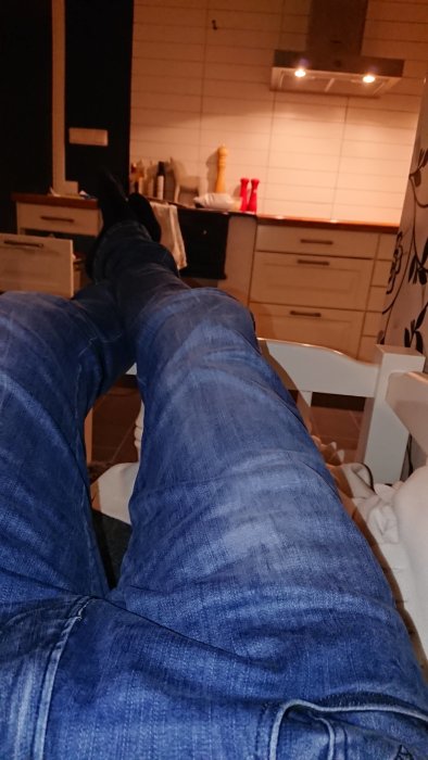 Personens ben uppsträckta på ett sofflock med köksinredning i bakgrunden.