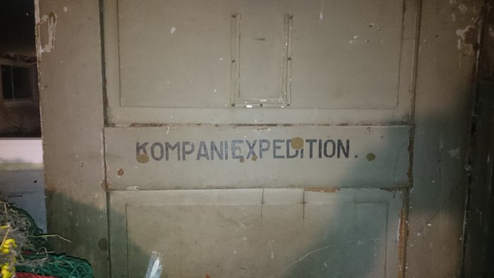 Sliten grå dörr med texten 'KOMPANIEEXPEDITION.' i vit färg som troligen är från ett militärt regemente.