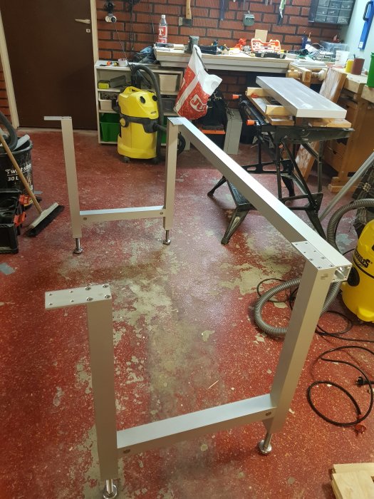 Monterad metallbenställning för ett bord i en verkstad med diverse verktyg och material i bakgrunden.