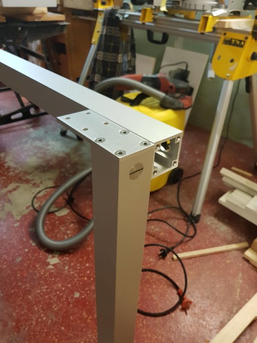Metallben för byggprojekt monterad i verkstadsmiljö med verktyg och träbitar i bakgrunden.