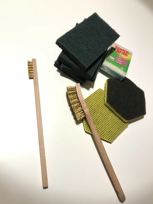 Slipmaterial inklusive skursvampar, slipplattor och sandpapper ligger utspridda på ett vitt bord.