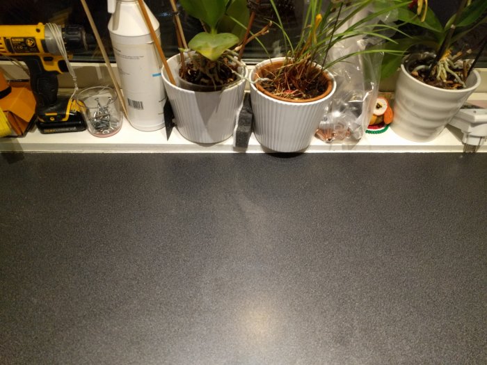 Köksbänk med laminatyta och växtkrukor framför fönster, verktyg och skruvar på bänken.