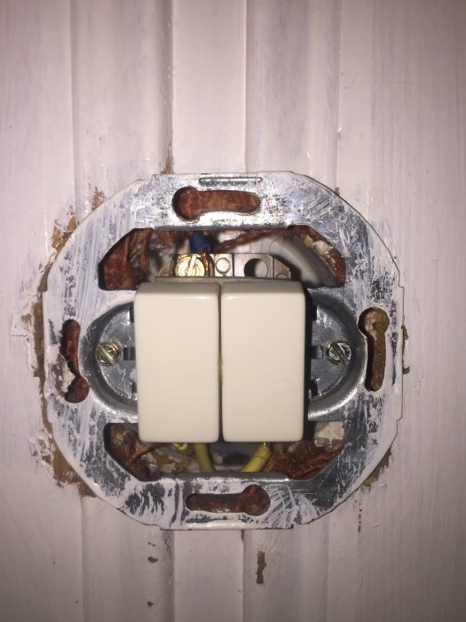 En öppen ljusströmbrytare med synliga gula och blå kablar i en vägg med vit panel.