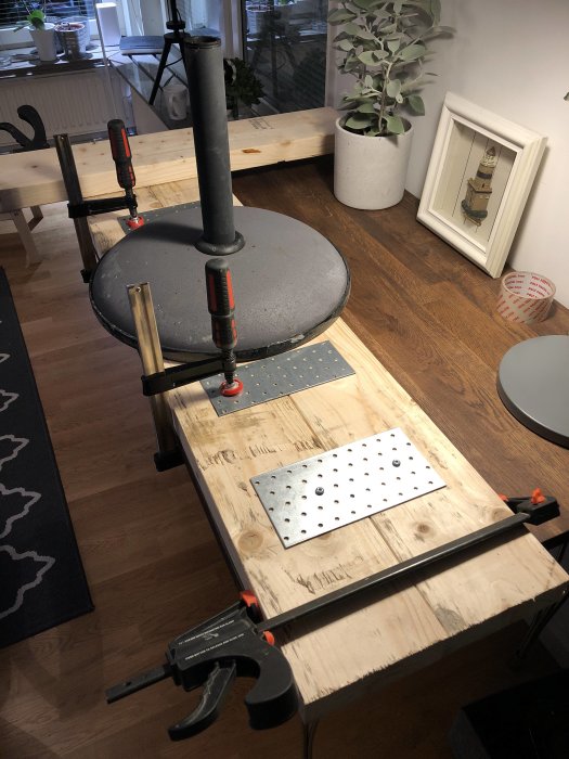DIY-projekt med träbrädor sammanfogade med klämmor och hålplåtar med vikter för stabilitet, ej fullständig limning synlig.