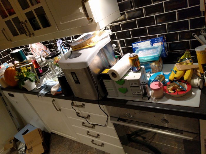 Kök med ny valnötsskiva och rörigt på bänken med brödrost, bananer och köksredskap.