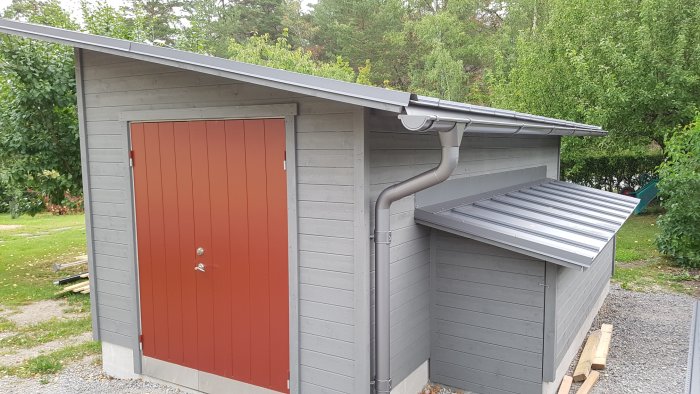 Nyinstallerat plåttak och takränna på en liten grå träbyggnad med röd dörr.