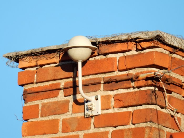 Gammal vit ventilationssvamp på tegelskorsten med trasslig kabel och getingbo.