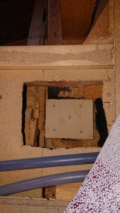 En träbit monterad på en gammal syll under ett hål i golvet, omgiven av kablar och murverk.