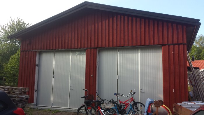 Nästan färdig rödmålad fasad på byggnad med vita garageportar och cyklar framför.