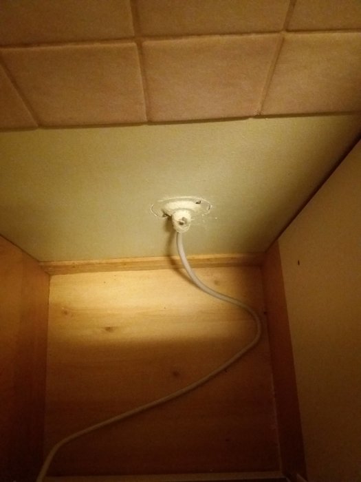 En sladd hänger från ett tomt eluttag i ett köksskåp.