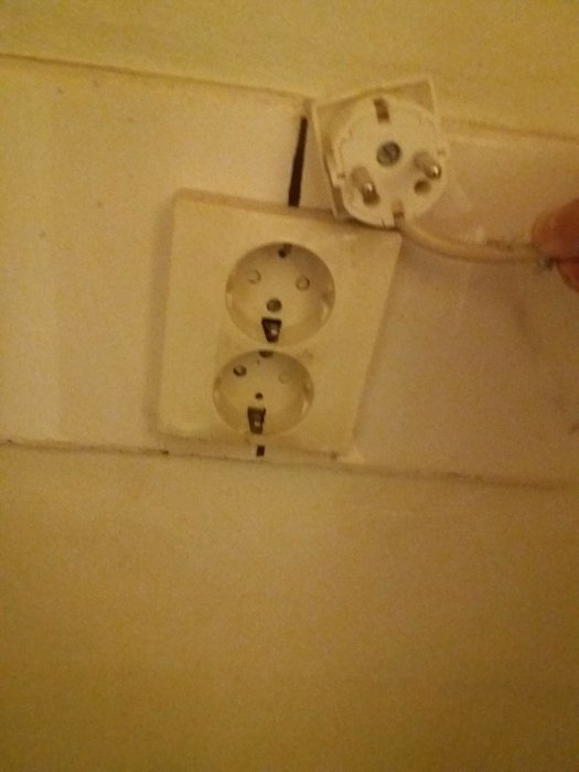 En hand kopplar en elkabel till ett öppet utanpåliggande dubbelvägguttag.