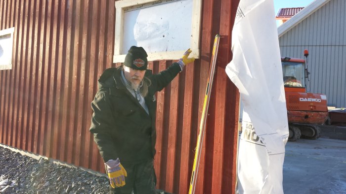 Man som håller en mätlina mot en röd byggnad på en byggarbetsplats under konstruktion.