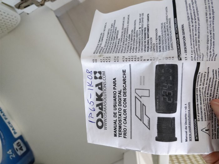 Hand som håller en instruktionsmanual för en termisk regulator med en bild av enheten.