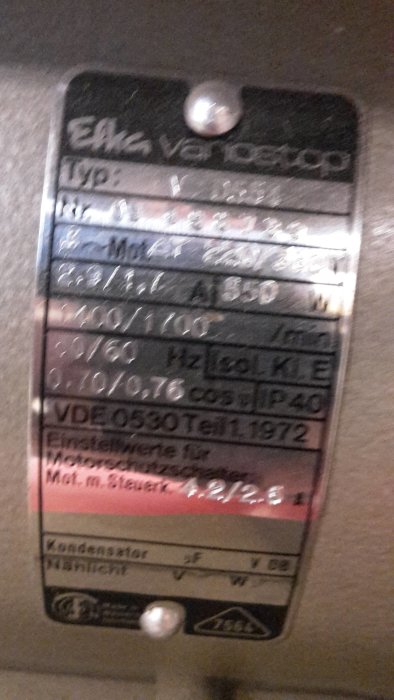 Otydligt foto på en metallskylt med teknisk information om en elektrisk maskin.
