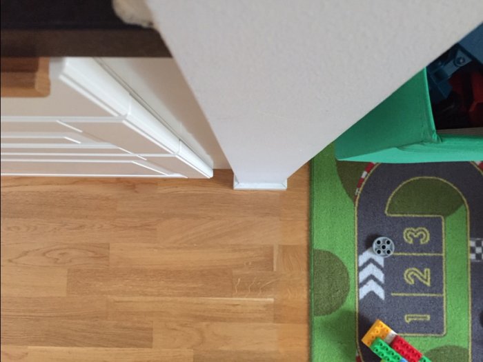 Parkettgolv med barnmatta och del av en vit dörrkarm synlig, detaljer i köksrenovering diskuteras.