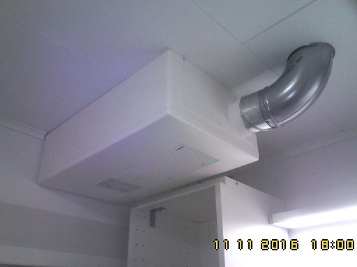 En FTX-ventilationsenhet installerad i taket i ett hörn av ett rum, med ansluten böjd ventilationskanal.