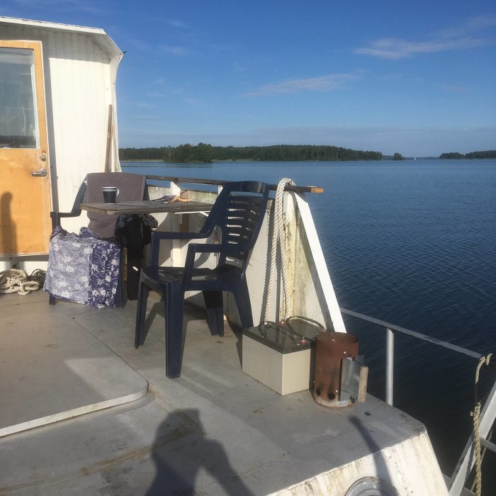 Utsikt från båtens akterdäck med stol och bord, skog och öppet vatten i bakgrunden.