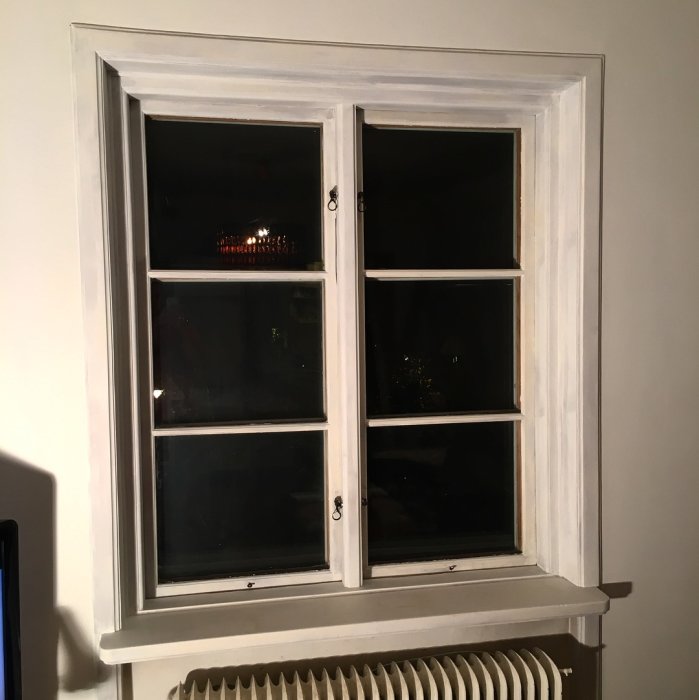 Nyslipat och grundmålat dubbelfönster i vitt med öppna spärrbeslag och nattvy utomhus.