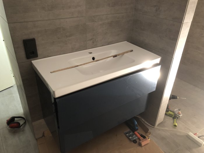Modernt svart tvättställ med vit topp under installation i ett gråkaklat badrum, byggverktyg synliga.