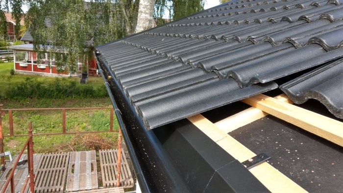 Nylagd svart takpanneplåt på ett hus med träställning och grannhus i bakgrunden.