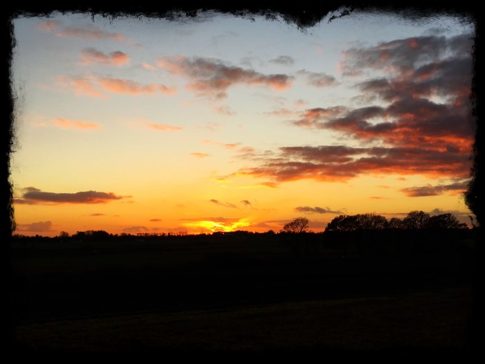 Dramatisk solnedgång med orange och röd himmel över ett silhuetterat landskap.