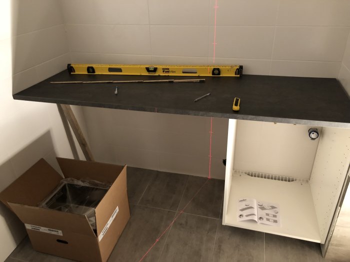 Ett modifierat Ikea-skåp utan dörrar med en omonterad bänkskiva ovanpå och en vattenpass, i ett rum under renovering.