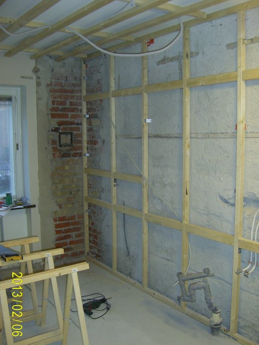 Pågående renovering med synliga vattenrör, roterande rasp och delar av köksinredning i en obebyggd lokal.