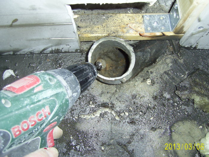 En borr används för att rengöra ett avkapad rör som sticker upp ur golv, nära köksinredningen.