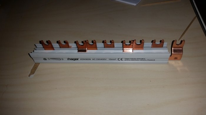 Kopparskena för elcentral med flera urtag för säkringar, märkt med Hager-logotypen, på ett bord.