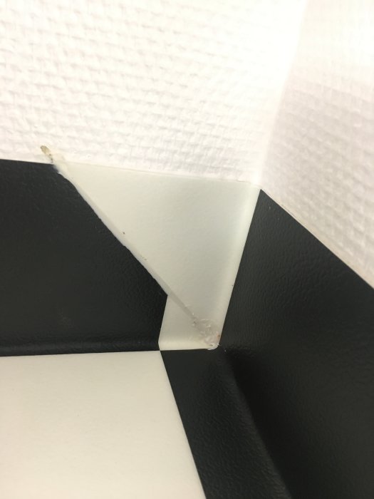 Dåligt utförd svetsning på hörnet av svart och vit golvbeläggning med synlig söm och ojämnheter.