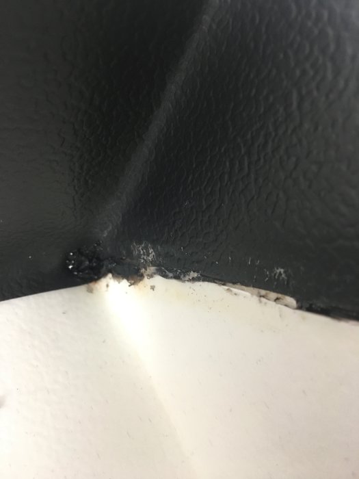 Golvmattans svetsning vid hörn med synliga brister och missfärgningar.