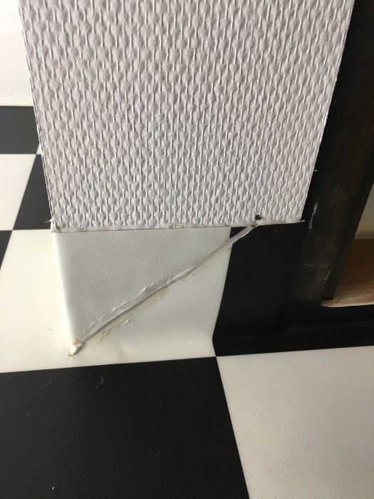 Dåligt utförda svetsningar och missfärgningar på rutig matta nära svart golvmatta i renoverat badrum.