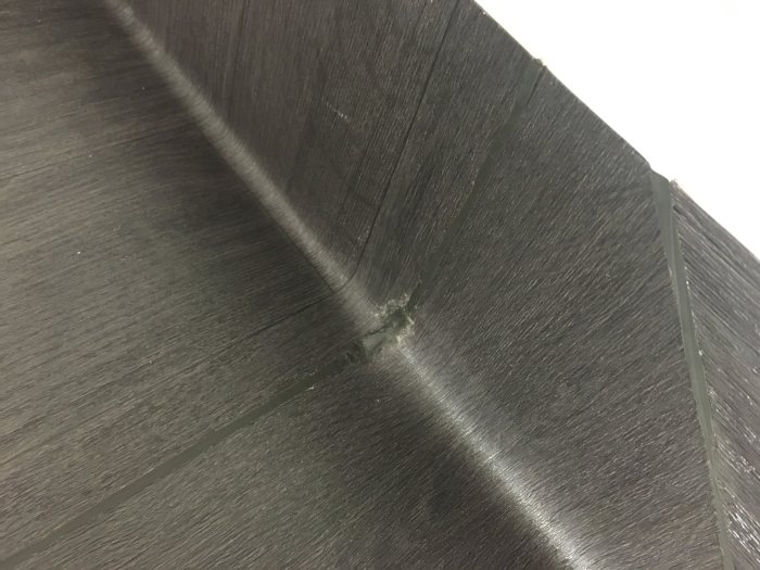 Svart golvbeläggning med synliga svetsningsskarvar och ojämn sammanfogning i ett hörn.