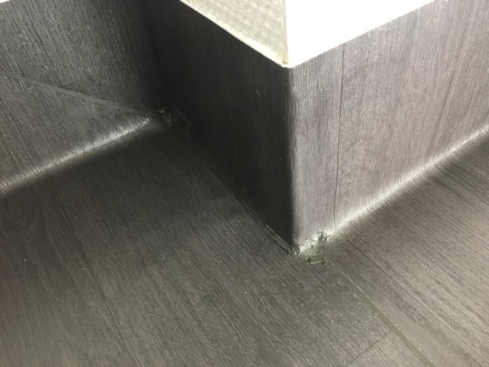 Svart golvbeläggning med slarvig svetsning och dålig finish vid hörn och kanter i ett renoveringsprojekt.