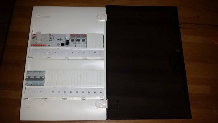 Elskåp med öppen dörr som visar säkringar och en jordfelsbrytare mot ett trägolv.