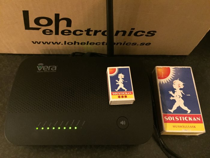 Vera Secure kontrollenhet för smart hem bredvid två tändsticksaskar på ett köksbord.