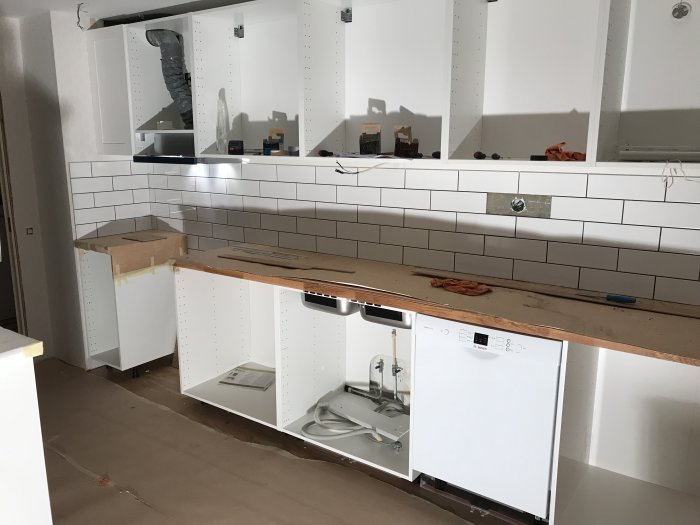 Kök under renovering med halvfärdigt kakelarbete och lösa vit kakellister på bänkskivan.