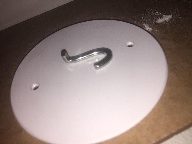 Vit takkrok fastskruvad i takuttag med rund form, placerad mot en mörk bakgrund.