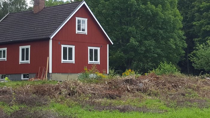 Renoverat rött hus med ny målning, nya fönster och foder, omgiven av grönska och byggmaterial.